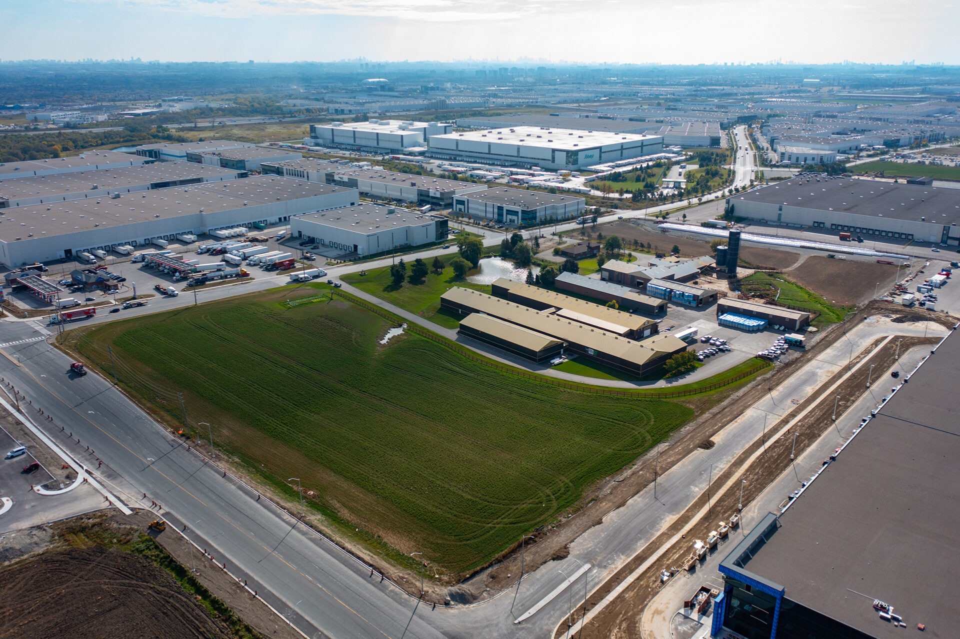 Aerial view of industrial area with large warehouses, roads, and green fields; no recognizable landmarks or historical buildings visible.