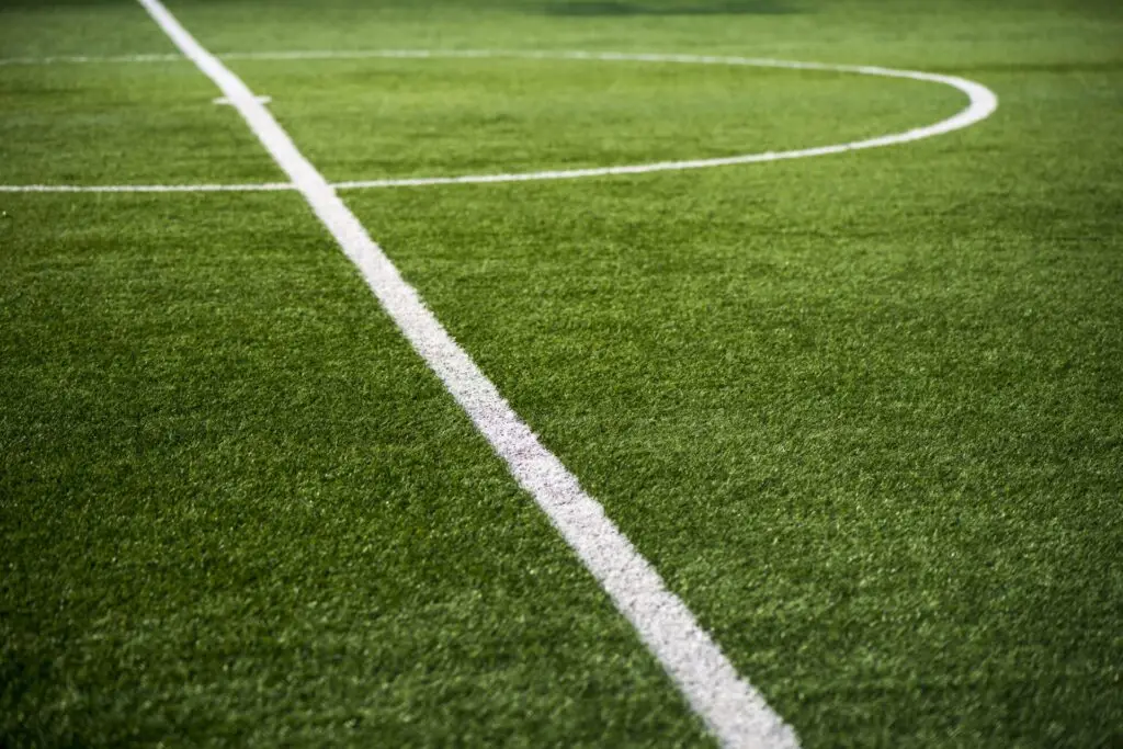 A close-up view of the center circle and lines on a green, well-maintained football field with no people present.
